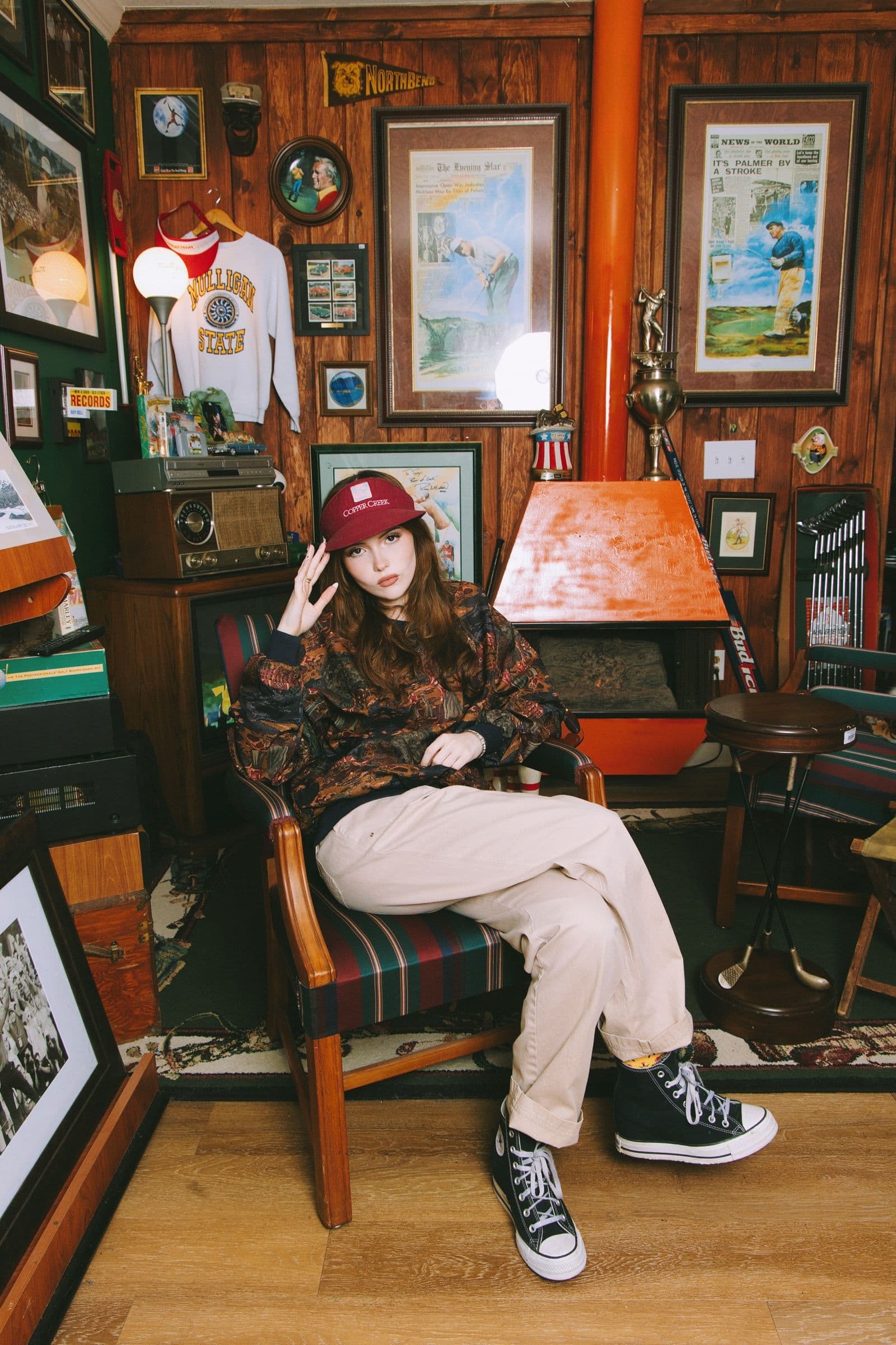 A model in a maroon Mulligan's bucket hat and vintage patterned top in a wood-paneled clubhouse room lined with framed vintage golf prints.