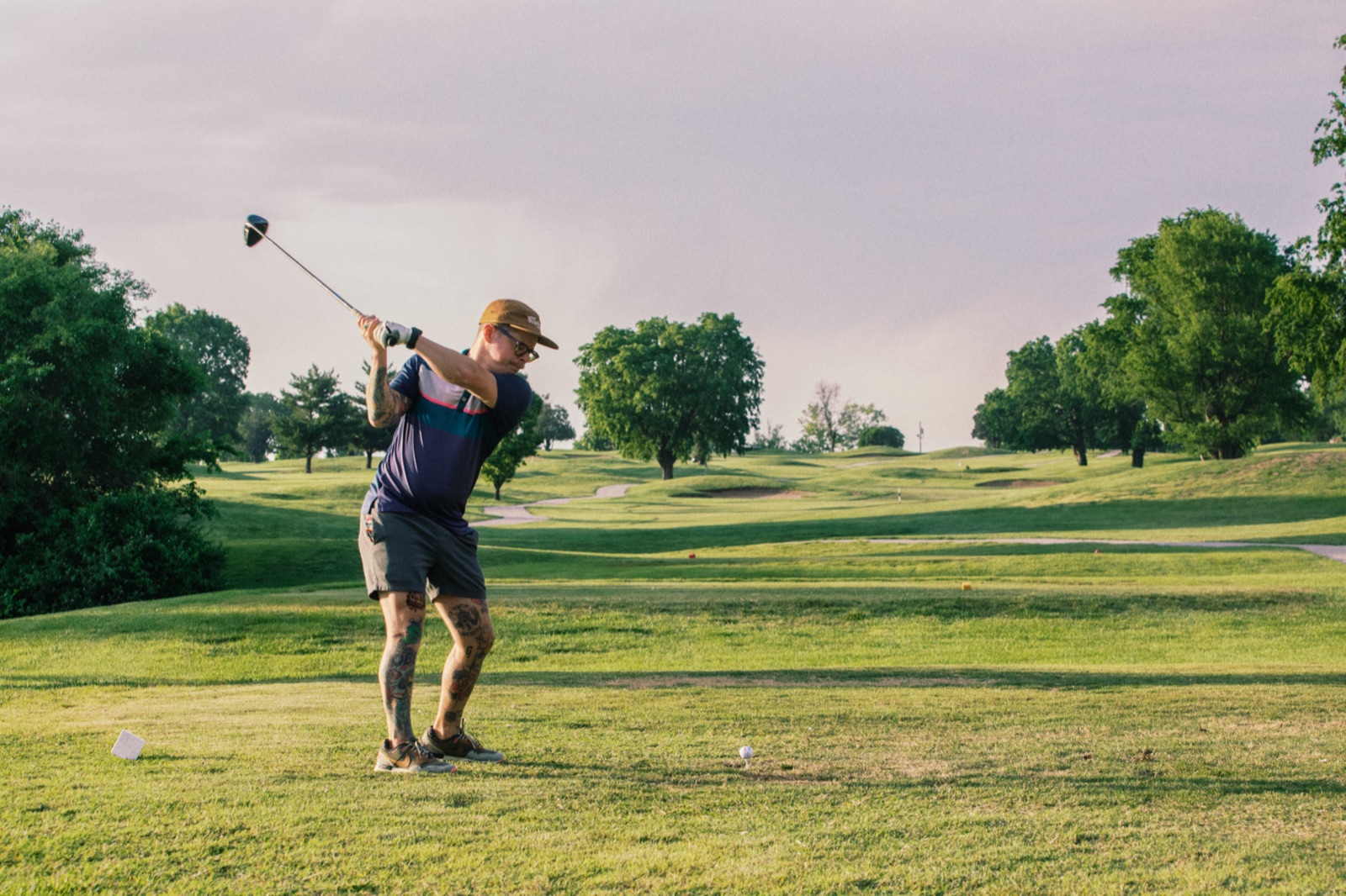 Driver swing against a pink sunset sky on the fairway