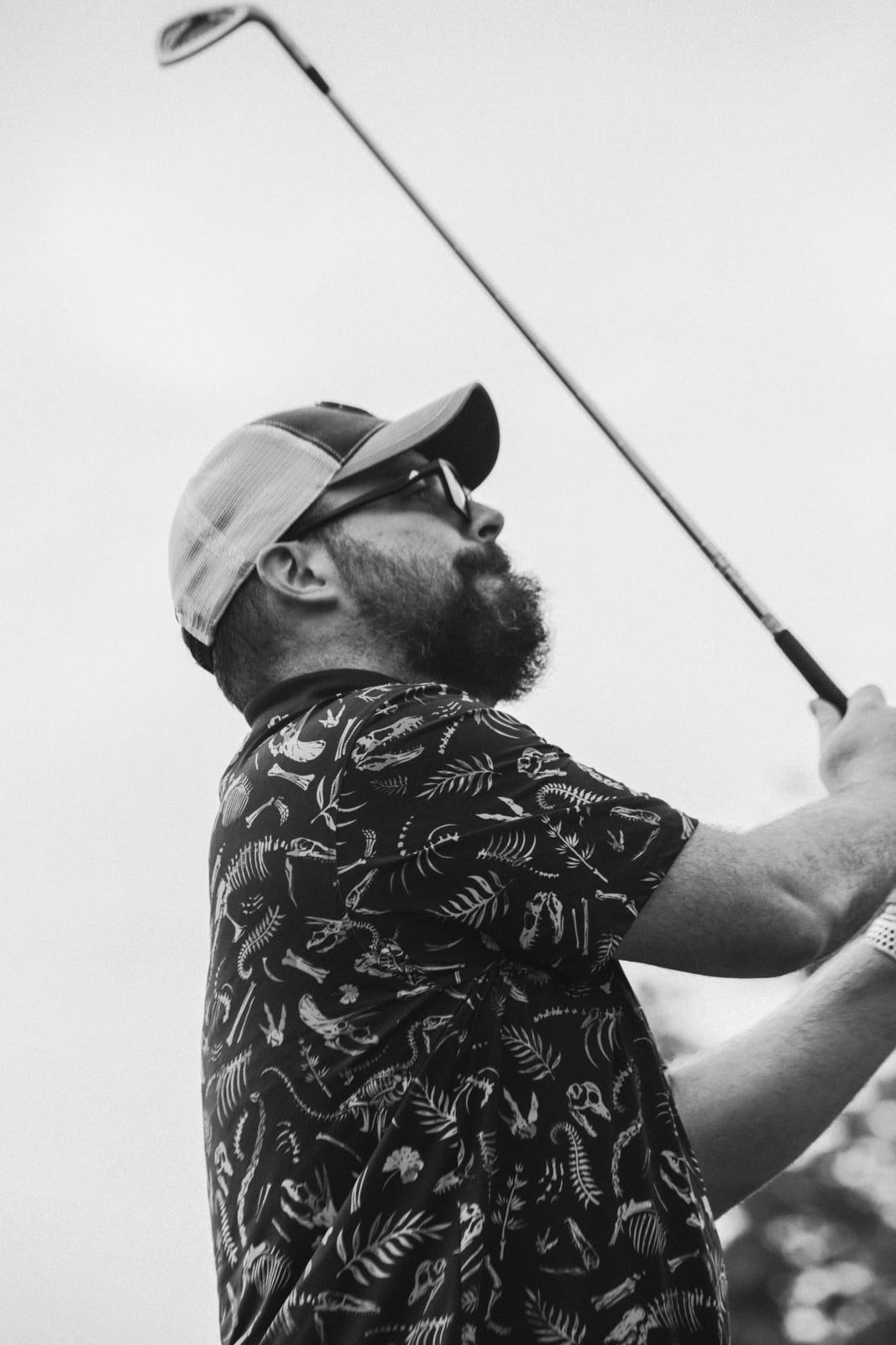 Golfer in a skeleton-print shirt watching his shot with his club held high
