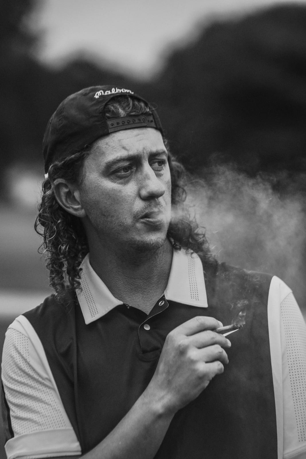 League member in a backwards Malbon cap exhaling smoke between holes