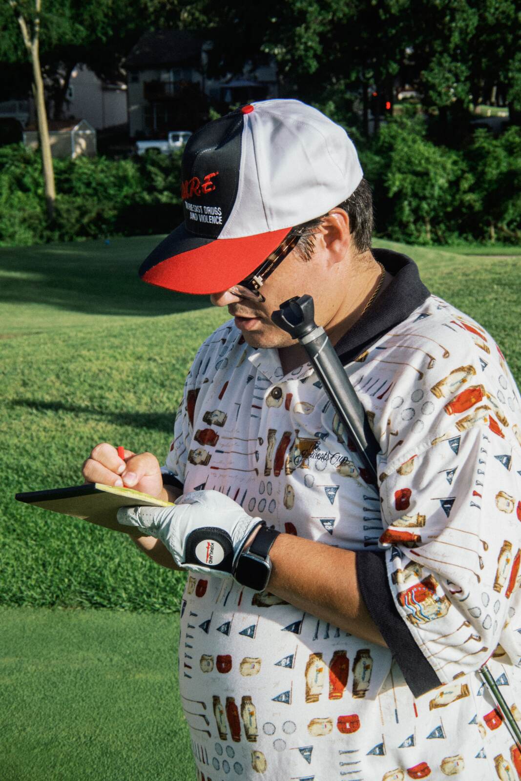 Player in an all-over-print shirt and a golf glove marking his scorecard