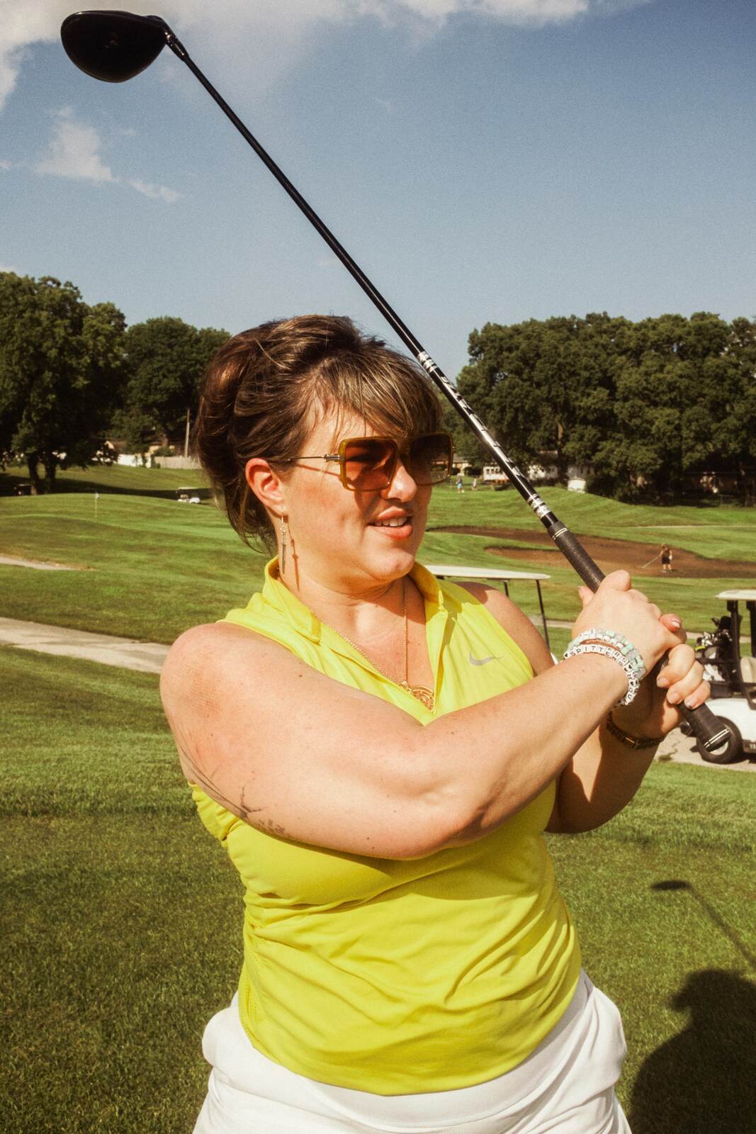 Golfer in a yellow polo at the top of her backswing with the driver