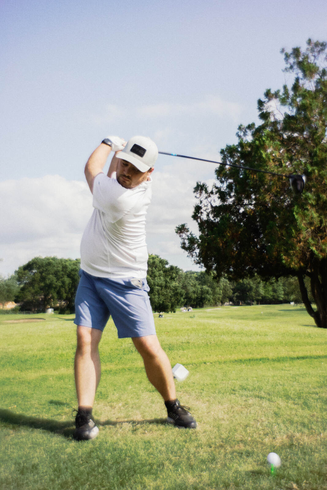 Player in a white tee and cap coiled at the top of his drive