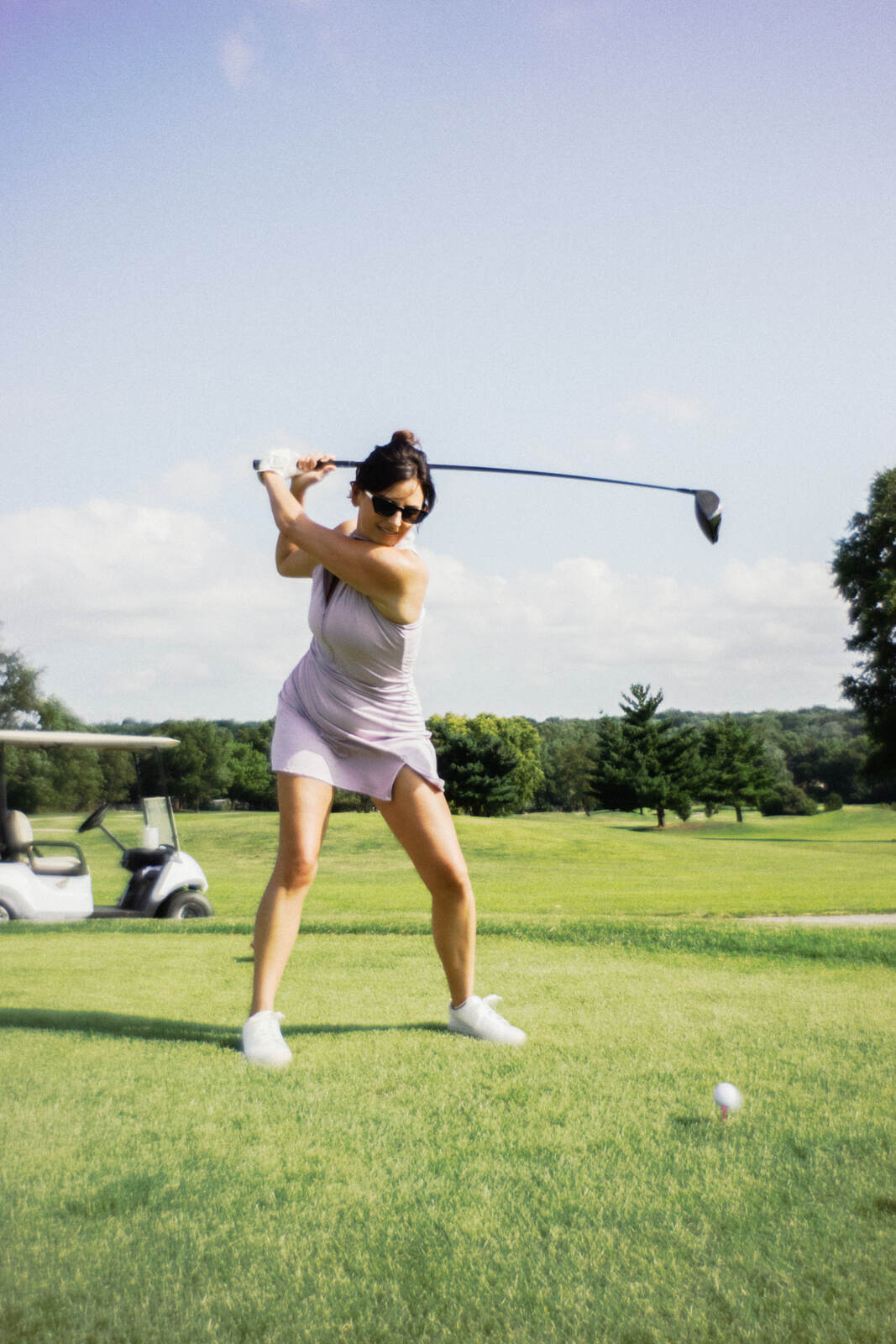Golfer in a lilac dress at the top of her backswing with the driver