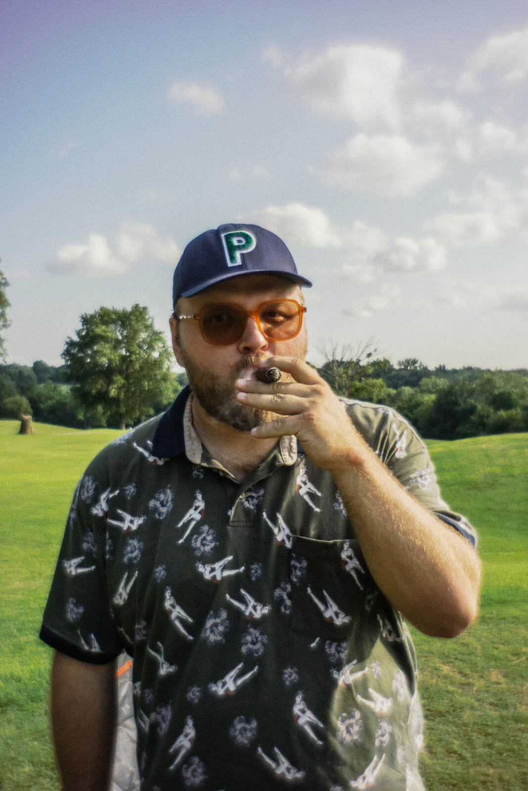 Player in a printed polo and orange tinted sunglasses with a cigar