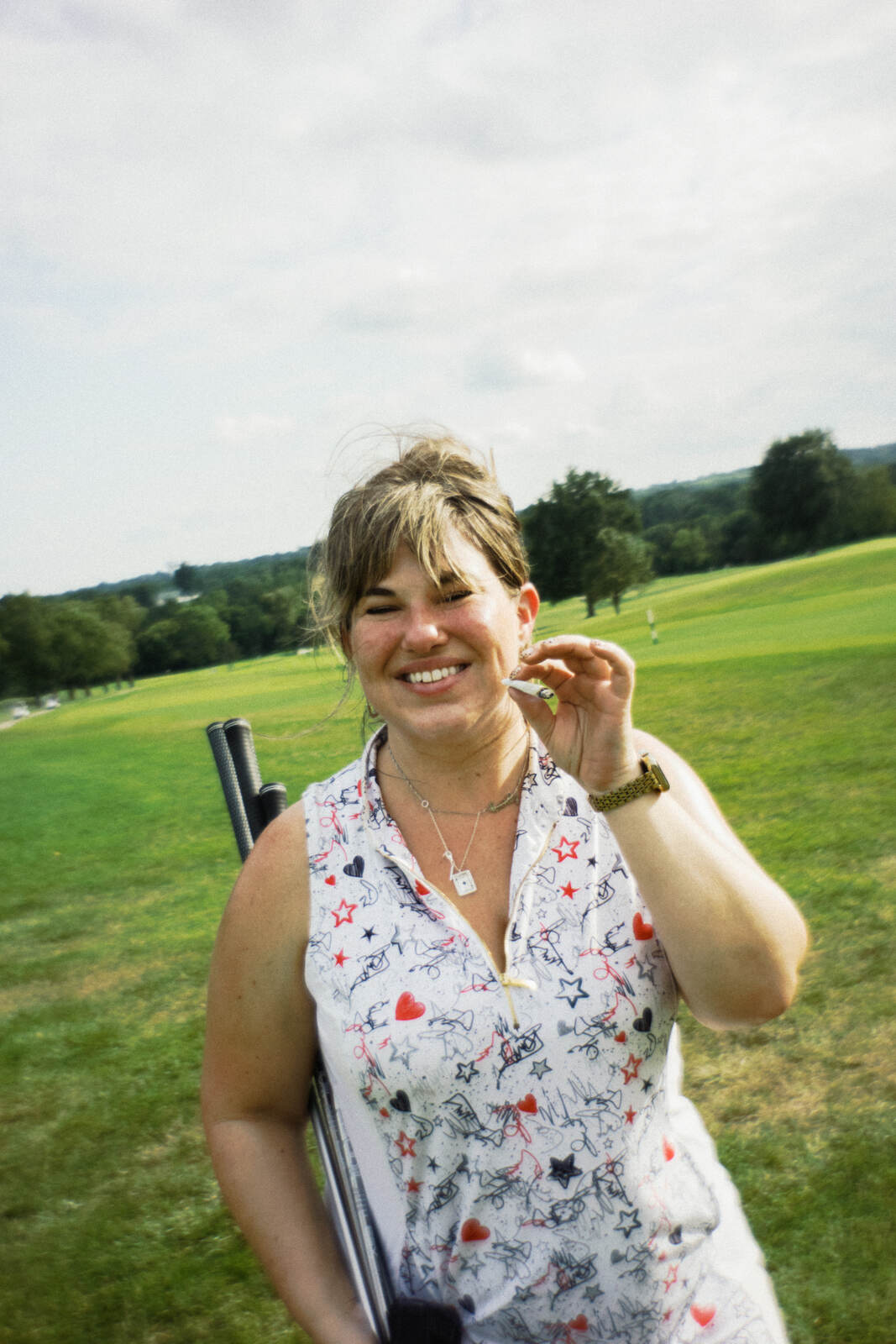 League member in a doodle print polo laughing with her clubs over her shoulder